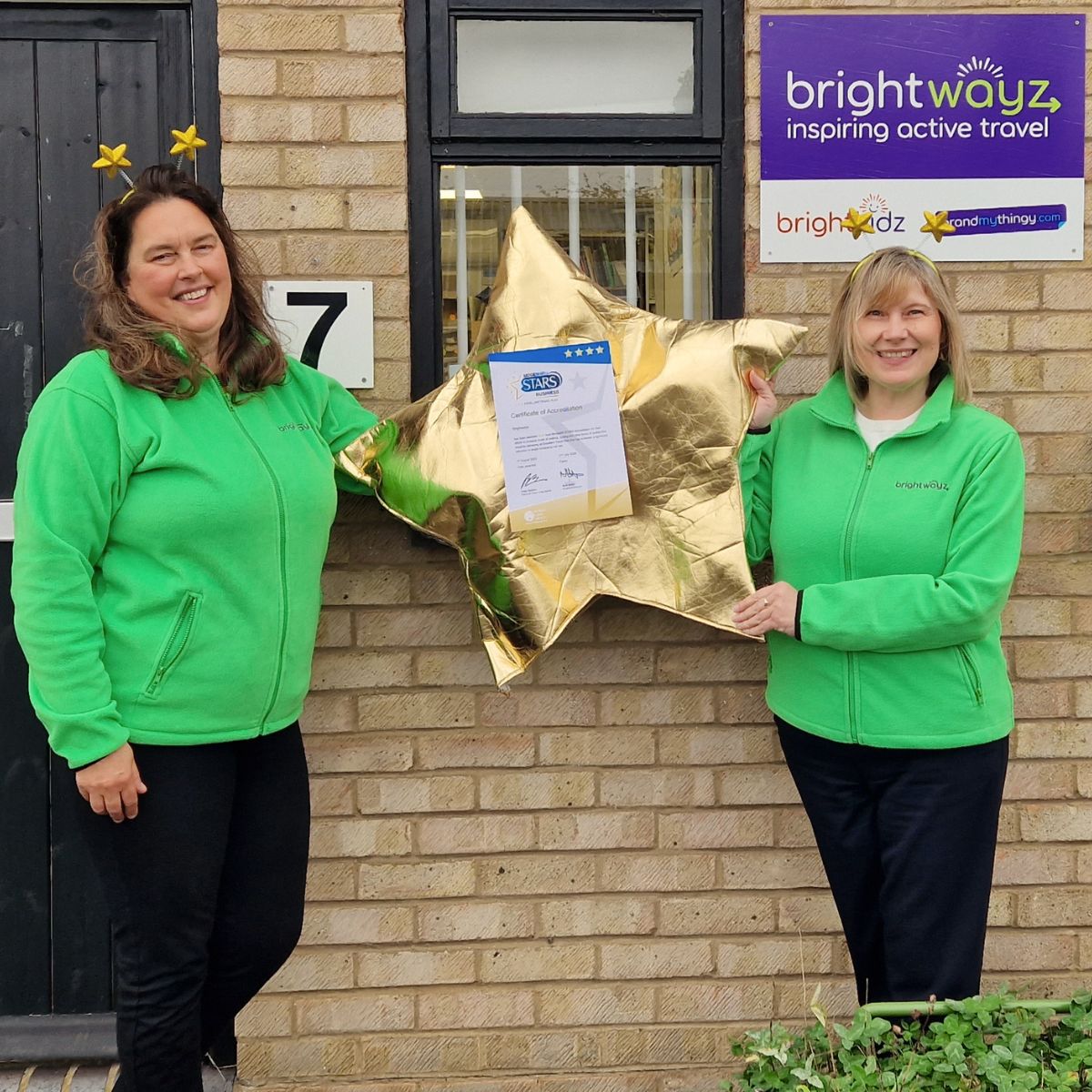 two Brightwayz team members holding a gold star and certificate with star head boppers